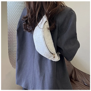 Detail of white embossed floral crossbody bag with gold hardware on a grey blazer