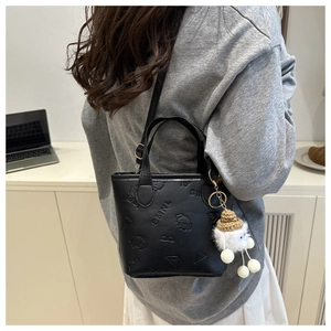 Détail d'un mini sac seau noir avec motifs embossés et un porte-clé en peluche blanc