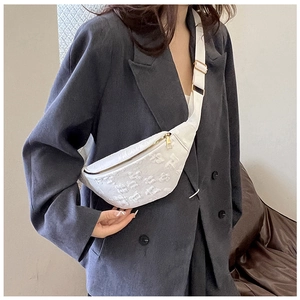 Close-up of white floral embossed crossbody saddle bag on model with gold hardware