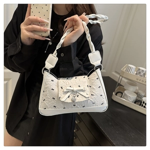 Detail of white underarm bag with black bow print and braided handle held by a model