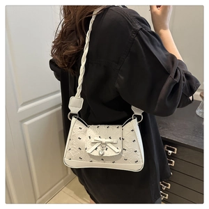 Close-up of white underarm bag with black bow patterns and silver heart pendant detail