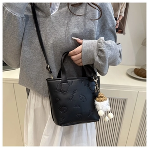 Détail d'un mini sac seau noir avec motifs en relief et pendentif en peluche