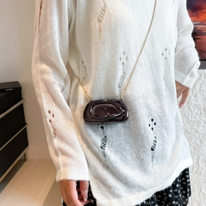 Modern glossy dark brown crossbody bag with gold chain strap shown on a model