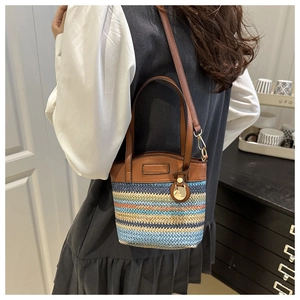 Detail of the woven straw bucket bag with colorful stripes and brown leather strap