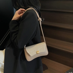 Petit sac rétro beige avec rabat pailleté et boucle dorée sur un blazer noir élégant