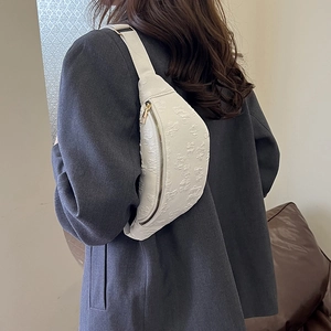 Borsa a sella beige con fiori a rilievo indossata come tracolla su un blazer grigio