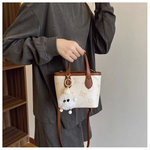 Detail of butterfly embossed handbag with plush charm and dark brown leather strap