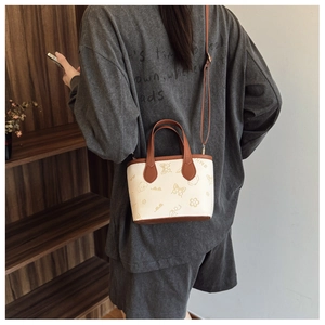 Model wearing a small cream crossbody bucket bag with brown trim and cute embossed patterns