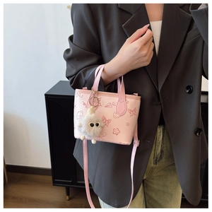Pink mini tote bag with playful cartoon prints and plush ball charm on a grey blazer