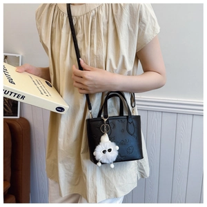 Detail of a black leather bucket bag with cartoon embossing and a fuzzy white charm