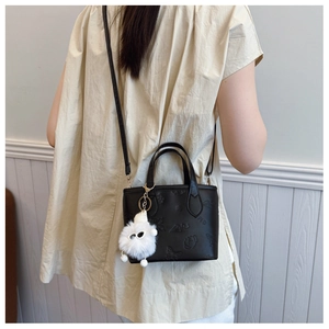 Detail of embossed black leather bucket bag with plush charm and crossbody strap