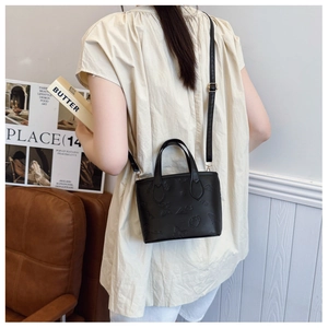 Detail of black embossed bucket bag with adjustable shoulder strap worn by a model