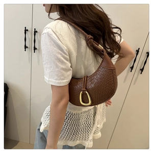 Brown woven crescent bag with gold horsebit hardware shown on a shoulder