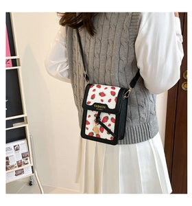 Detail of mini crossbody bag featuring red strawberry print and golden charm on model