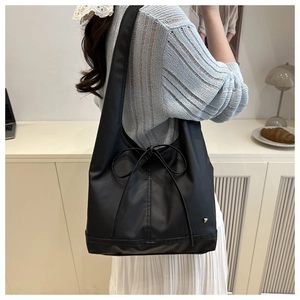 Detail der schwarzen Shopper-Tasche mit dekorativer Schleife und herzförmigem Metalldetail