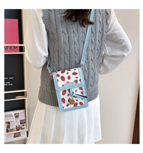 Detail of light blue floral crossbody bag with strawberry print and gold pendant decoration