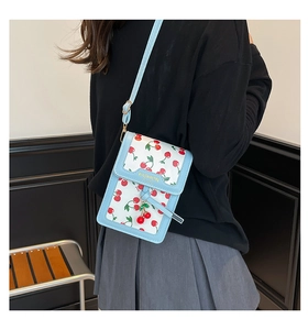Close-up of a light blue crossbody bag featuring red cherry prints and golden lettering