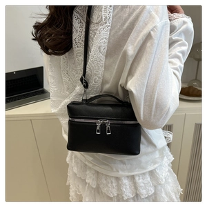 Black litchi grain leather crossbody bag shown on model's shoulder with lace top outfit