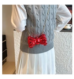 Detail of red bow-shaped crossbody bag with glossy finish and thin gold metal chain strap