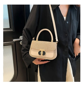 Detail of glitter-covered flap and gold clasp on a cream crossbody handbag worn by a model