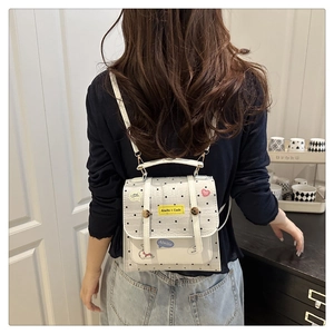 Detail of white polka dot backpack with colorful cartoon stickers and yellow logo tag
