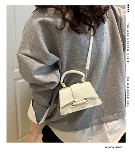 White mini crossbody bag with leather ring detail shown on model in a minimalist setting