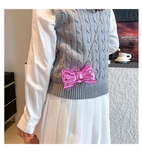 Chic glossy pink bow mini crossbody bag with gold chain strap on a stylish model outfit