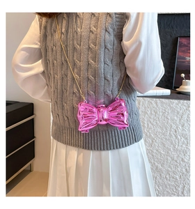 Detail of a bright pink bow-shaped crossbody bag with a gold metal chain strap