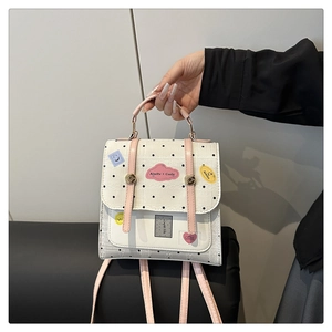 Close-up of a white polka dot mini backpack with pink straps and cute cartoon prints