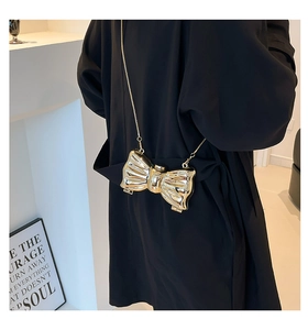 Glossy golden bow-shaped mini chain bag shown as a stylish accessory on a black coat