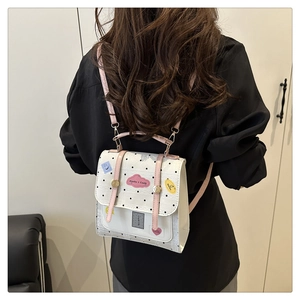 Detail of white polka dot backpack with pink leather straps and colorful cartoon patches