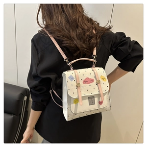 Detail of a white polka dot mini backpack with pink straps and cute cartoon patches