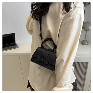 Close-up of black mini crossbody bag with litchi texture and gold hardware on a desk