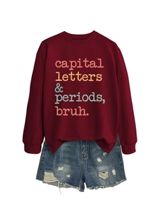 Flat lay of a dark red sweatshirt with 'capital letters' text and ripped denim shorts