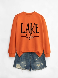 Close-up of LAKE life graphic lettering on orange crewneck sweatshirt with denim shorts