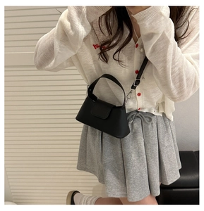 Detail of a black matte leather baguette bag with top handle and adjustable strap