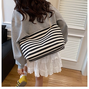 Rear view of a model wearing the black and white striped canvas tote with gold chain strap