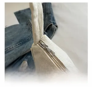 Detailed close-up of a silver zipper on a cream corduroy bag with a Fashion woven label
