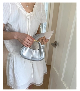 Detail of silver half-moon bag with metallic mirror finish and golden ring handle