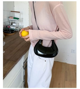Detail of black glossy patent leather crescent shoulder bag worn by model in a daily scene