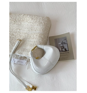 Nahaufnahme einer weißen Halbmondtasche aus Lackleder mit goldenen Metallteilen im Bett