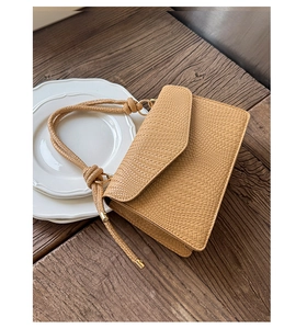 Détail du sac bandoulière camel en cuir tressé avec bandoulière corde sur table en bois