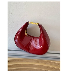 Detail of wine red patent leather shoulder bag with gold hardware and curved crescent shape