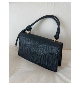 Détail du sac à main noir tressé avec poignée à nœud et anneaux métalliques dorés