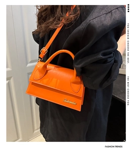 Detail view of bright orange crossbody bag with gold metal logo and textured leather finish