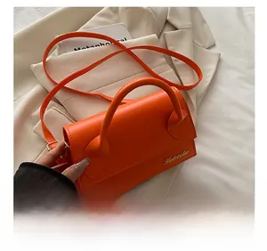 Detail van helder oranje PU-leren crossbodytas met goudkleurig logo op een beige pak