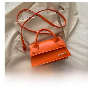 Detailopname van oranje leren mini tas met gouden letters en telefoon ter referentie van de maat