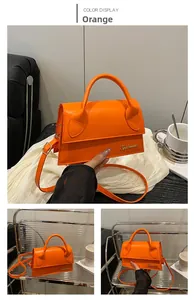 Detail view of orange leather handbag with metal logo and adjustable crossbody strap