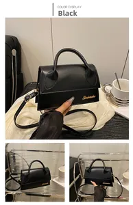 Detail of black textured PU leather handbag with gold metal lettering and top handle