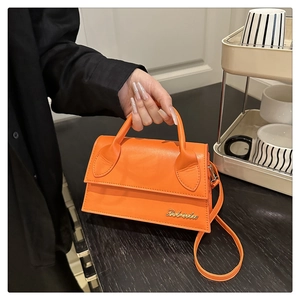 Vue détaillée du sac à main en cuir orange vif avec logo métallique et poignée courbe